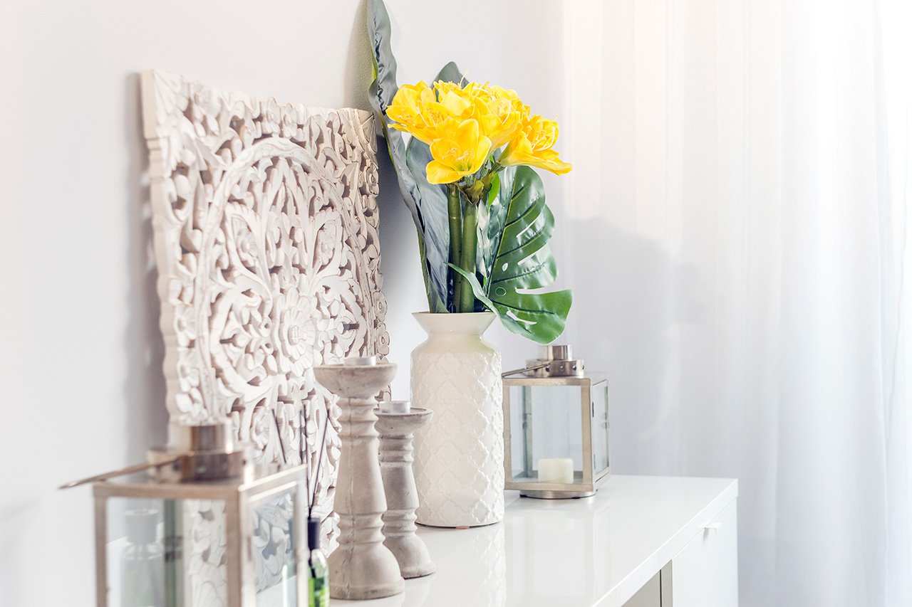 Yellow flowers in ceramic vase with wooden candlesticks and lantern decorating a shelf